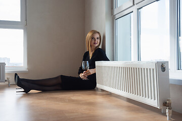 Image showing girl with a beautiful smile and a glass of wine sitting on the floor