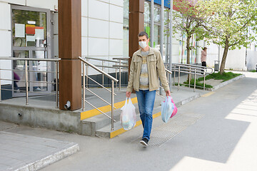 Image showing a man in a medical mask walks down an empty street with shopping