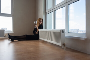 Image showing girl thoughtfully stares into a large window with a glass of wine in her hand