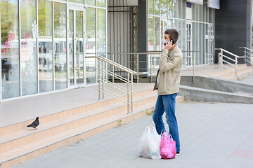 Image showing a man in a medical mask in the street talking on the phone standing in front of the store