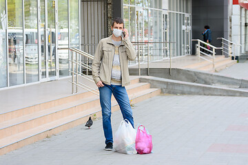 Image showing a man in a medical mask stands on the street shopping and talks on his mobile phone