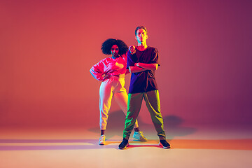 Image showing Stylish man and woman dancing hip-hop in bright clothes on gradient background at dance hall in neon light