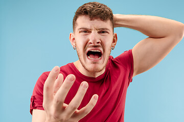 Image showing The young emotional angry man screaming on blue studio background