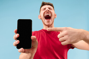 Image showing Young handsome man showing smartphone screen isolated on blue background in shock with a surprise face