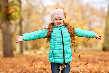 Image showing happy girl playing with leaves at autumn park