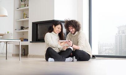 Image showing multiethnic couple using tablet computer in front of fireplace