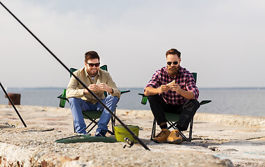 Image showing happy friends fishing and eating sandwiches