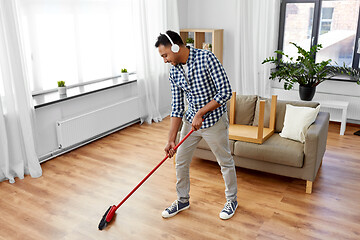 Image showing man in headphones with broom cleaning at home