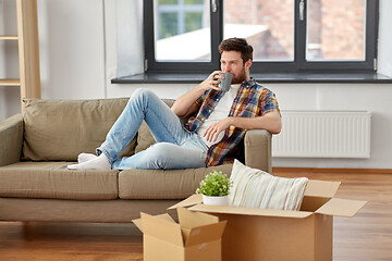 Image showing man with boxes and drinking coffee at new home