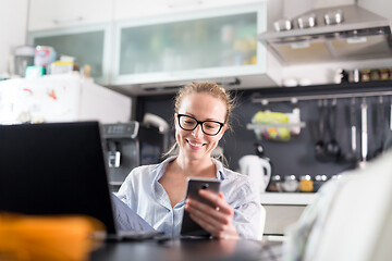 Image showing Stay at home and social distancing. Woman in her casual home clothing working remotly from kitchen dining table. Video chatting using social media with friend, family, business clients or partners