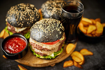 Image showing Homemade delicious black burgers served on wooden cutting board with ketchup, potato wedges