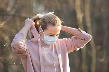 Image showing Portrait of caucasian sporty woman wearing medical protection face mask while walking in park, relaxing and listening to music. Corona virus, or Covid-19, is spreading all over the world