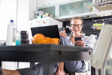 Image showing Stay at home and social distancing. Woman in her casual home clothing working remotly from kitchen dining table. Video chatting using social media with friend, family, business clients or partners