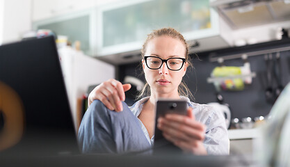 Image showing Stay at home and social distancing. Woman in her casual home clothing working remotly from kitchen dining table. Video chatting using social media with friend, family, business clients or partners