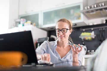 Image showing Stay at home and social distancing. Woman in her casual home clothing working remotly from kitchen dining table. Video chatting using social media with friend, family, business clients or partners