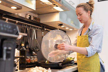 Image showing Stay at home housewife woman cooking in kitchen, stir frying dish in a saucepan, preparing food for family dinner.