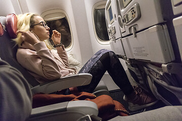 Image showing Sporty casual young blonde caucasian lady watching movie while traveling by airplane by the window. Commercial transportation by planes