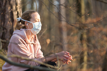 Image showing Portrait of caucasian sporty woman wearing medical protection face mask while relaxing in nature and listening to music. Corona virus, or Covid-19, is spreading all over the world