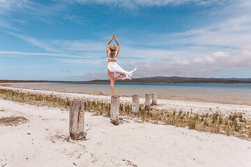 Image showing Beautiful woman balance on wooden post yoga pose in swimwear and sarong