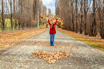 Image showing Woman throwing leaves in air in front of heart of fallen leaves 