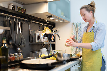 Image showing Stay at home housewife woman cooking in kitchen, stir frying dish in a saucepan, preparing food for family dinner.