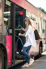 Image showing Teenage girl commuter entering city bus carring foldable electric urban scooter, wearing protective face mask against spreading of coronavirus and disease transmission at time of covid-19 pandemic