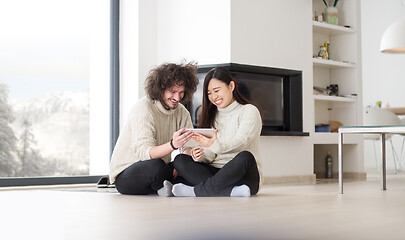 Image showing multiethnic couple using tablet computer in front of fireplace