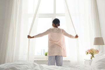 Image showing happy african american woman opening curtains