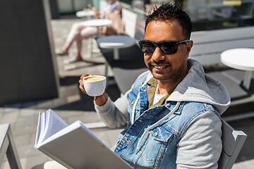 Image showing man reading book and drinking coffee at city cafe