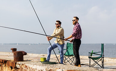 Image showing male friends with fishing rods on sea pier