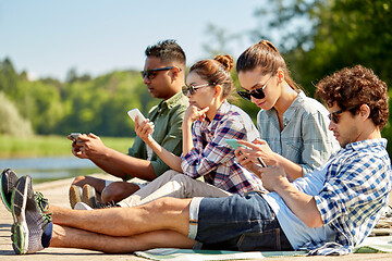 Image showing friends with smartphone on lake pier in summer