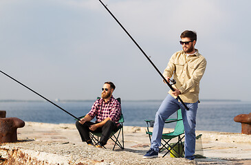 Image showing male friends with fishing rods on sea pier