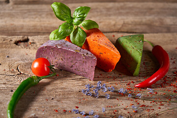 Image showing Three different cheeses on rough wooden planks: lavender, paprika and pesto cheeses