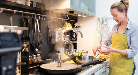Image showing Stay at home housewife woman cooking in kitchen, salting dish in a saucepan, preparing food for family dinner.