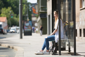 Image showing Casual caucasian teenager commuter with modern foldable urban electric scooter sitting on a bus stop bench waiting for metro city bus. Urban mobility concept