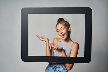 Image showing Happy excited teen girl looking through digital tablet frame and showing directing to blank copy space