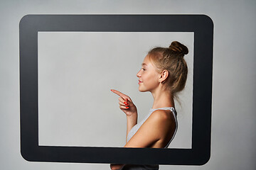 Image showing Profile of girl standing behind digital tablet frame and pointing a finger at blank copy space