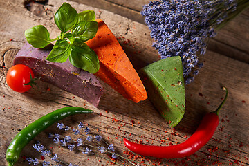 Image showing Three different cheeses on rough wooden planks: lavender, paprika and pesto cheeses