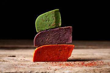 Image showing Three different cheeses on rough wooden planks: lavender, paprika and pesto cheeses