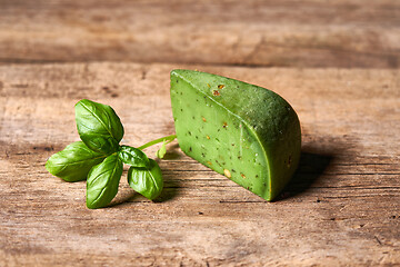 Image showing A piece of gourmet basil cheese with twig of basil on rough wooden planks