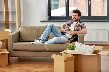 Image showing man with boxes and drinking coffee at new home
