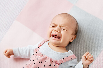 Image showing crying baby girl lying on knitted blanket