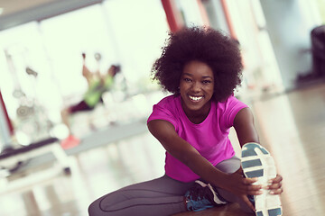 Image showing woman in a gym stretching and warming up man in background worki