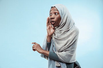 Image showing The young african woman whispering a secret behind her hand over blue background