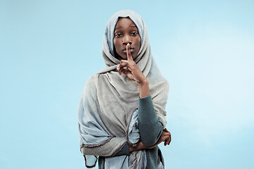 Image showing The young african woman whispering a secret behind her hand over blue background