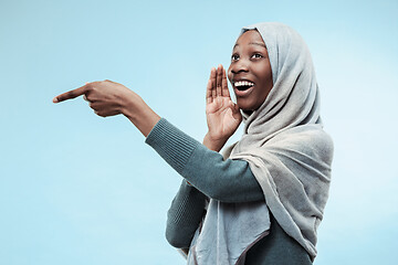 Image showing The young african woman whispering a secret behind her hand over blue background