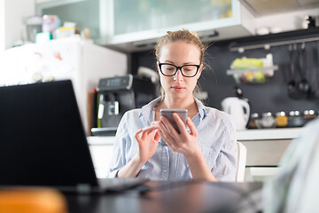 Image showing Stay at home and social distancing. Woman in her casual home clothing working remotly from kitchen dining table. Video chatting using social media with friend, family, business clients or partners