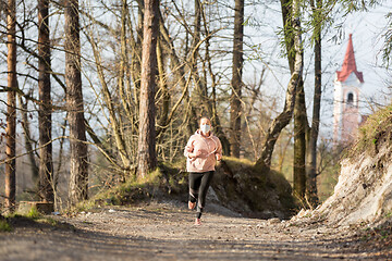 Image showing Corona virus, or Covid-19, is spreading all over the world. Portrait of caucasian sporty woman wearing a medical protection face mask while running in nature.