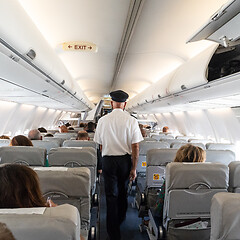 Image showing Interior of commercial airplane with flight attandant serving passengers on seats during flight. Steward in uniform walking the aisle.square composition