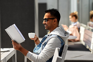 Image showing man reading book and drinking coffee at city cafe